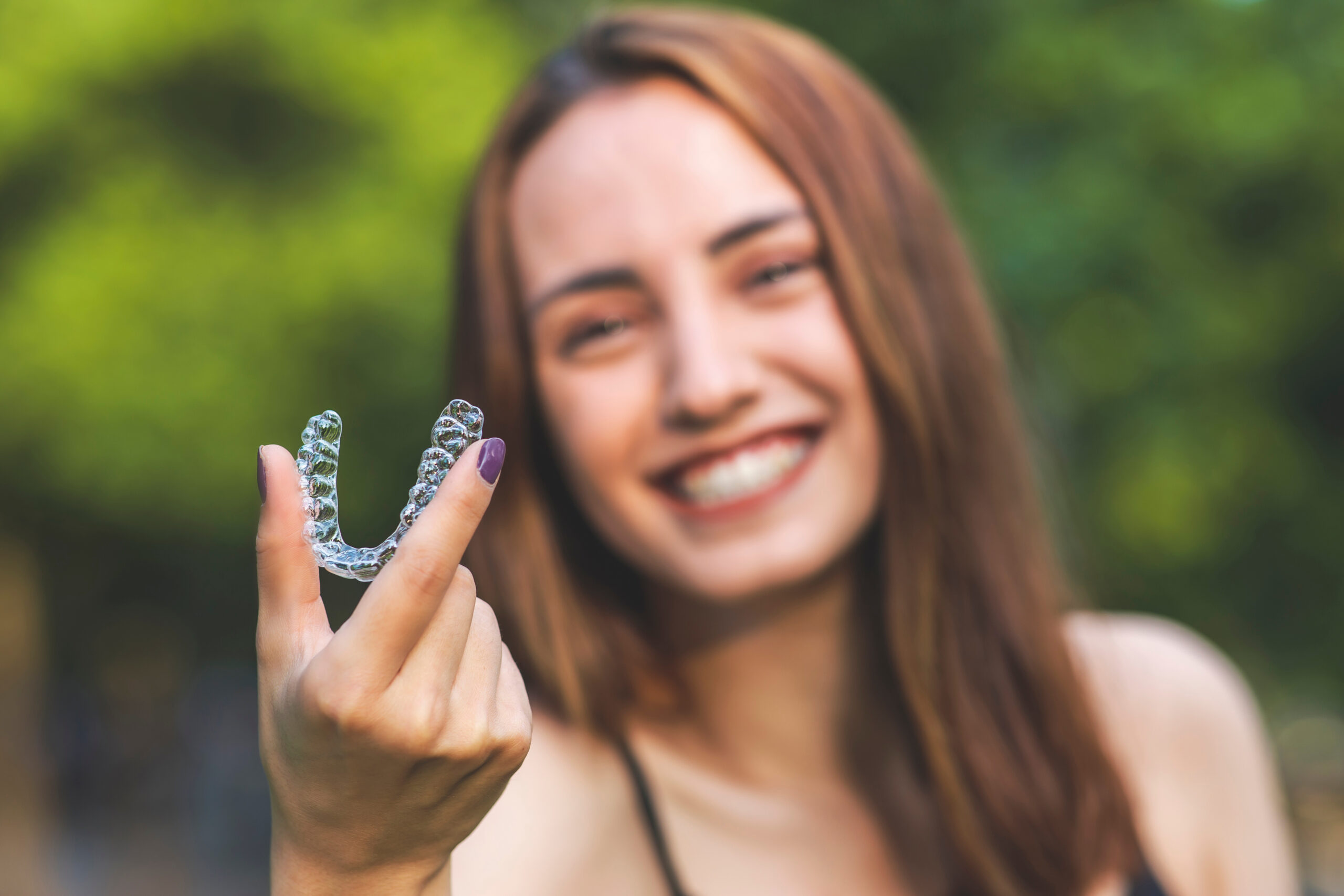 Beautiful smiling Turkish woman is holding an invisalign bracer Smiling woman holding a ClearCorrect clear aligner for invisible teeth straightening at The Center for Complete Healthy Dentistry, Connecticut's ClearCorrect specialists in Wilton, CT