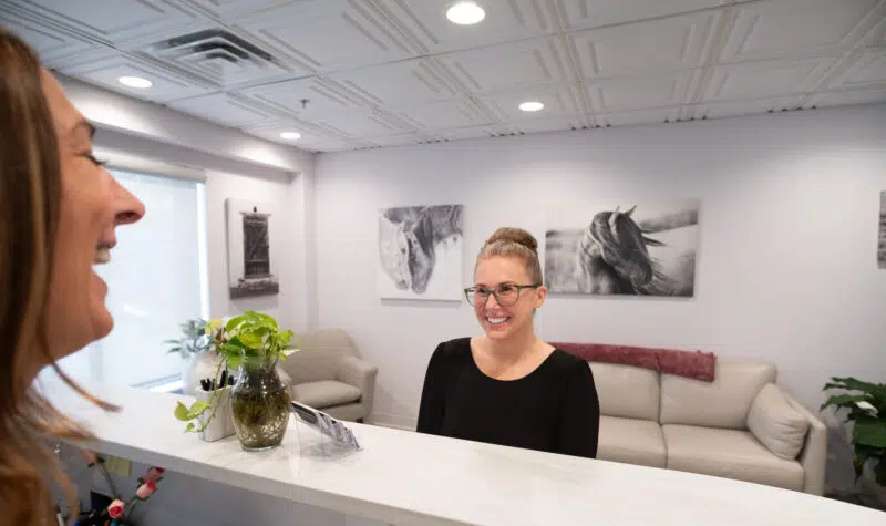 crown-bridgework-welcoming-front-desk-center-for-complete-healthy-dentistry-wilton-ct Friendly receptionist greeting a patient at the front desk for crown and bridgework services at The Center for Complete Healthy Dentistry in Wilton, CT