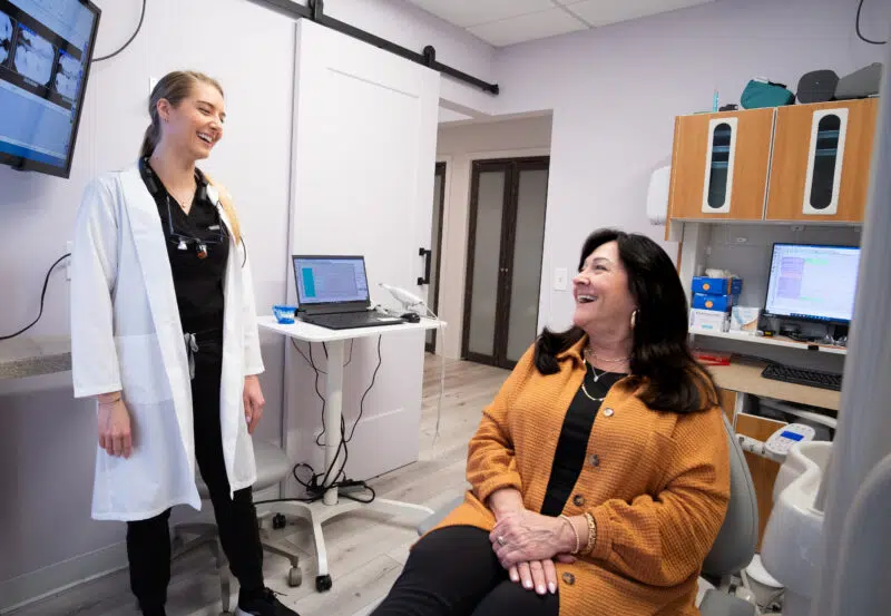 dental-team-member-with-patient-center-for-complete-healthy-dentistry-wilton-ct Friendly dental team member in white coat consulting with a smiling patient in the modern treatment room at The Center for Complete Healthy Dentistry in Wilton, CT