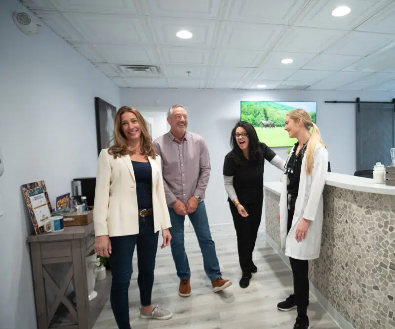 gum-disease-treatment-team-center-for-complete-healthy-dentistry-wilton-ct Friendly dental team and patients laughing together in the welcoming reception area at The Center for Complete Healthy Dentistry, providing gum disease treatment in Wilton, CT